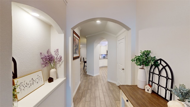 hallway with lofted ceiling, ornamental molding, and light hardwood / wood-style flooring