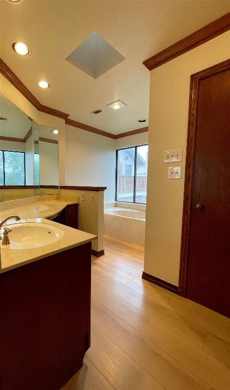 bathroom with vanity, a bathtub, wood-type flooring, and ornamental molding