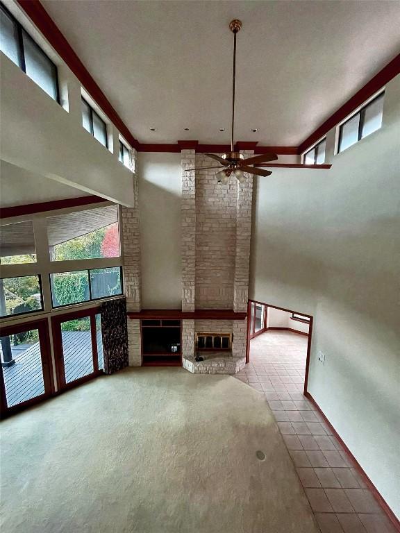 unfurnished living room featuring a brick fireplace, tile patterned floors, a towering ceiling, and ceiling fan