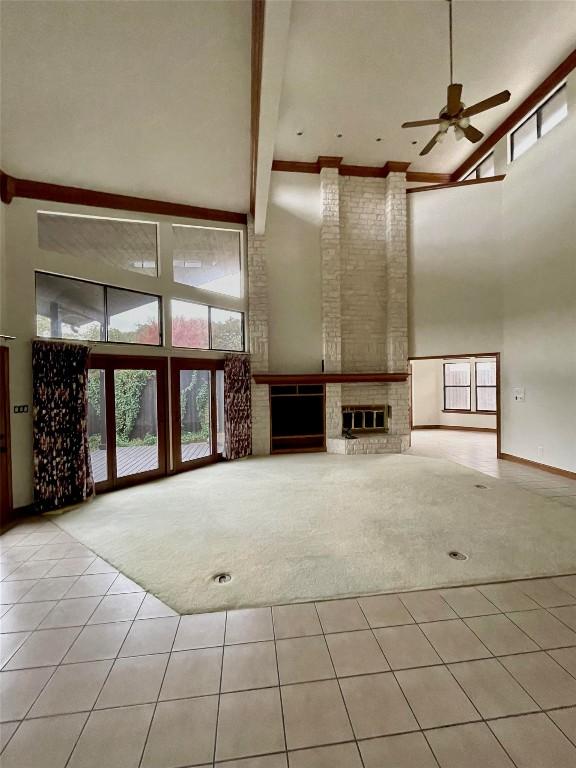 unfurnished living room featuring light tile patterned floors, ceiling fan, a high ceiling, a fireplace, and beamed ceiling