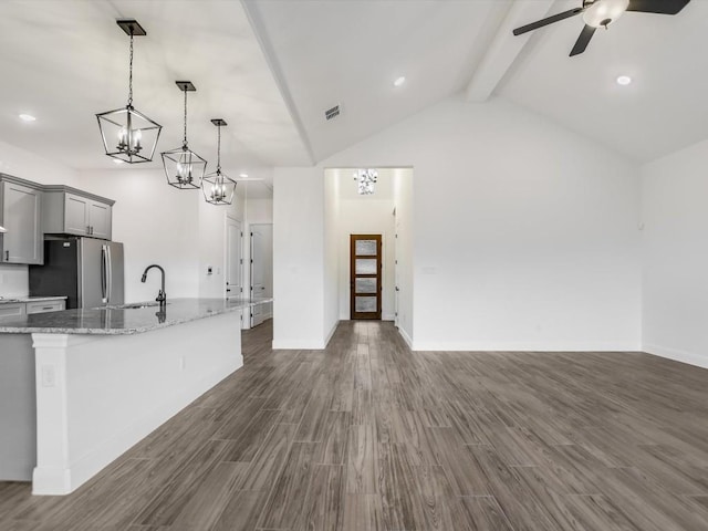 kitchen with gray cabinetry, hanging light fixtures, stainless steel fridge, light stone counters, and dark hardwood / wood-style flooring