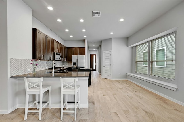 kitchen featuring sink, appliances with stainless steel finishes, a kitchen breakfast bar, decorative backsplash, and kitchen peninsula