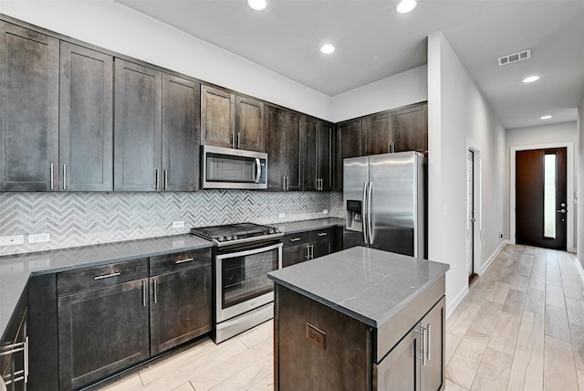 kitchen with appliances with stainless steel finishes, decorative backsplash, a center island, dark brown cabinets, and light hardwood / wood-style flooring