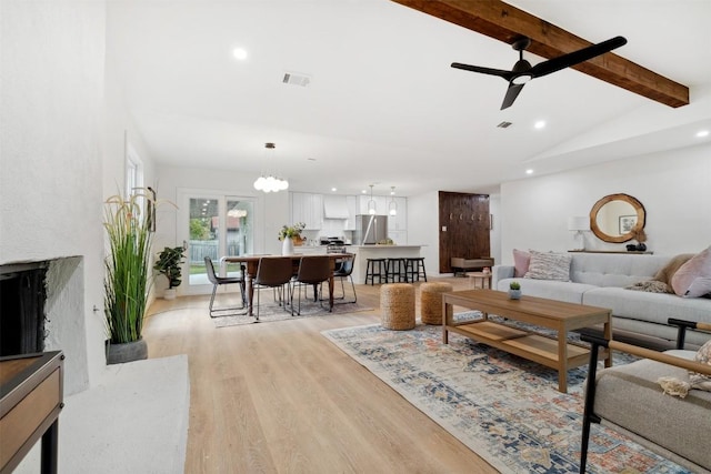 living room featuring vaulted ceiling with beams, light hardwood / wood-style floors, and ceiling fan with notable chandelier