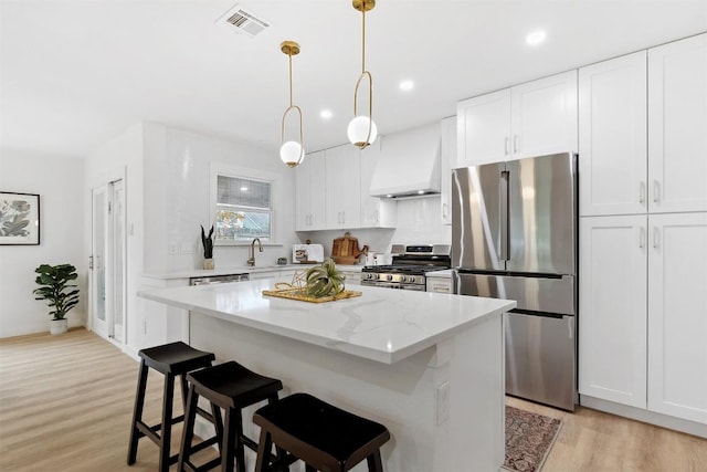 kitchen featuring a center island, premium range hood, appliances with stainless steel finishes, light stone counters, and white cabinetry