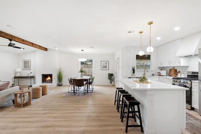 kitchen featuring a breakfast bar, stainless steel range with gas cooktop, light hardwood / wood-style flooring, ceiling fan, and white cabinetry