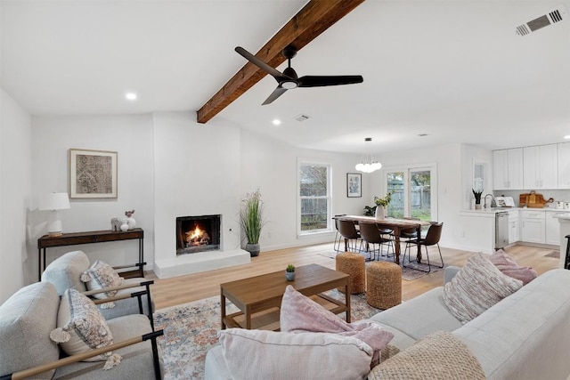 living room featuring lofted ceiling with beams, light wood-type flooring, and ceiling fan with notable chandelier