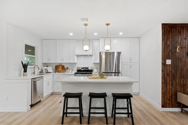 kitchen featuring light hardwood / wood-style flooring, a kitchen island, pendant lighting, and appliances with stainless steel finishes