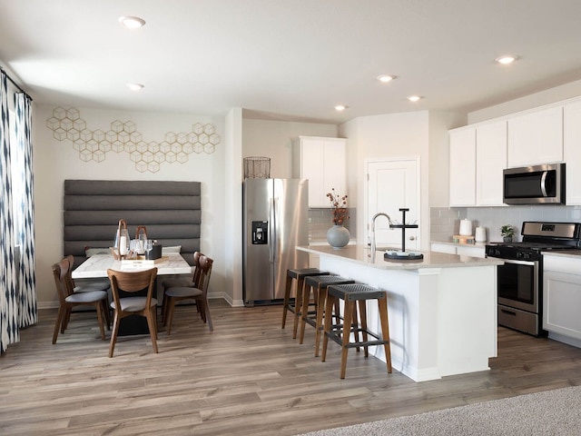 kitchen featuring appliances with stainless steel finishes, tasteful backsplash, white cabinetry, and a center island with sink