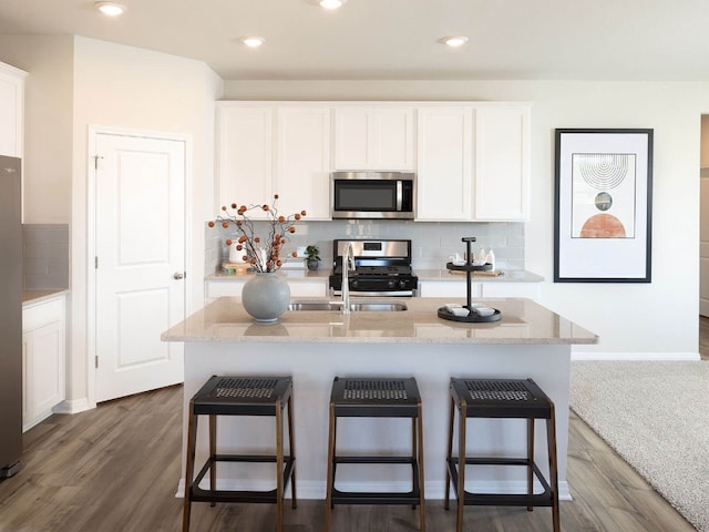 kitchen with stainless steel appliances, white cabinets, decorative backsplash, and a kitchen island with sink