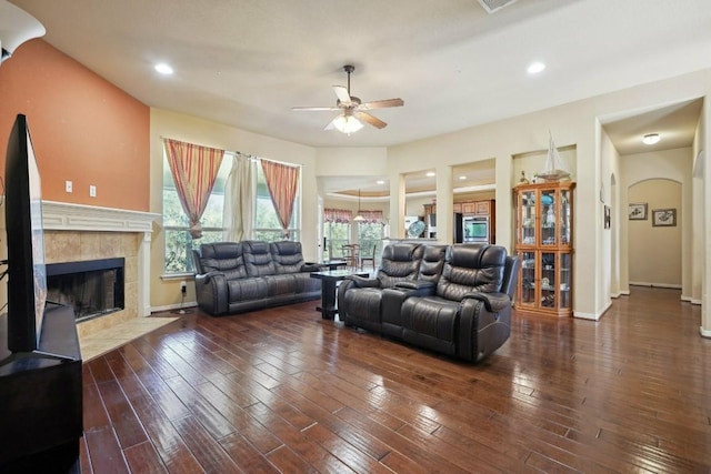 living room featuring ceiling fan, dark wood-type flooring, and a tiled fireplace