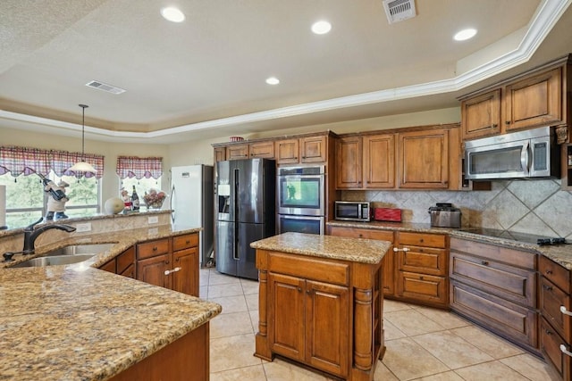 kitchen with sink, ornamental molding, appliances with stainless steel finishes, a tray ceiling, and a kitchen island