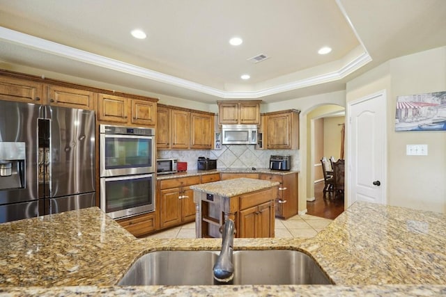 kitchen with light stone countertops, decorative backsplash, stainless steel appliances, sink, and a center island