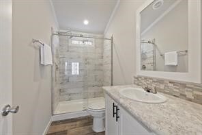 bathroom with vanity, a shower with door, backsplash, toilet, and wood-type flooring