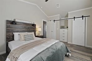 bedroom with a barn door, crown molding, wood-type flooring, and vaulted ceiling