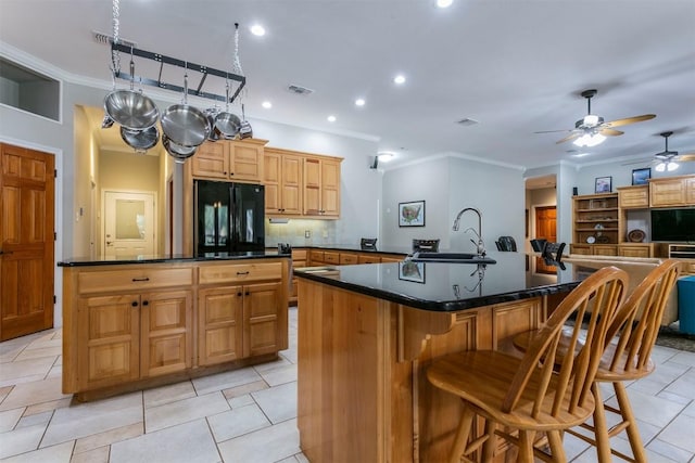 kitchen featuring black refrigerator, backsplash, ornamental molding, sink, and a large island with sink