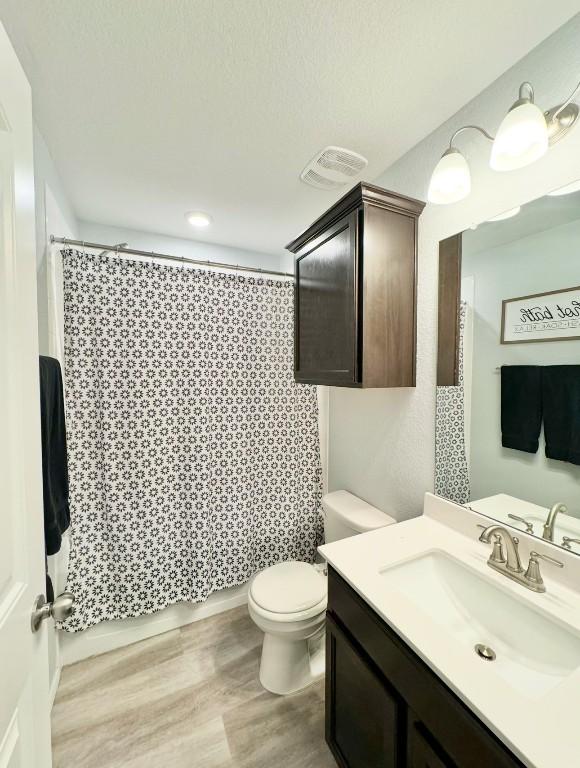 bathroom with hardwood / wood-style flooring, vanity, toilet, and walk in shower