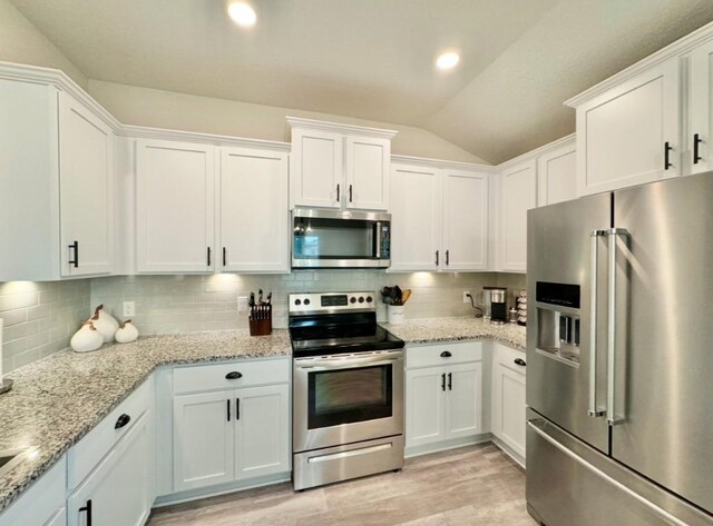 kitchen with tasteful backsplash, lofted ceiling, white cabinets, light stone counters, and stainless steel appliances