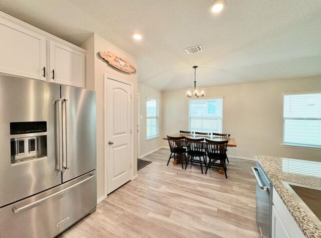 kitchen with light stone countertops, white cabinetry, appliances with stainless steel finishes, and light wood-type flooring