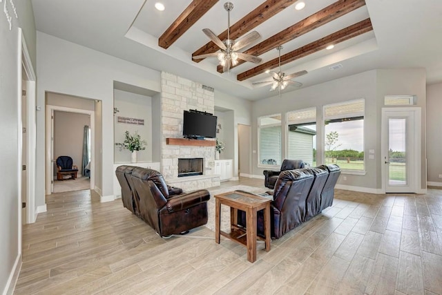 living room featuring beam ceiling, light hardwood / wood-style flooring, ceiling fan, and a stone fireplace