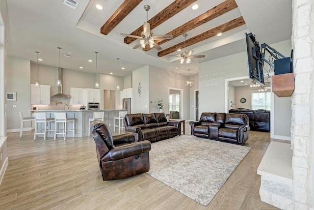 living room featuring beam ceiling, ceiling fan, a towering ceiling, and light wood-type flooring