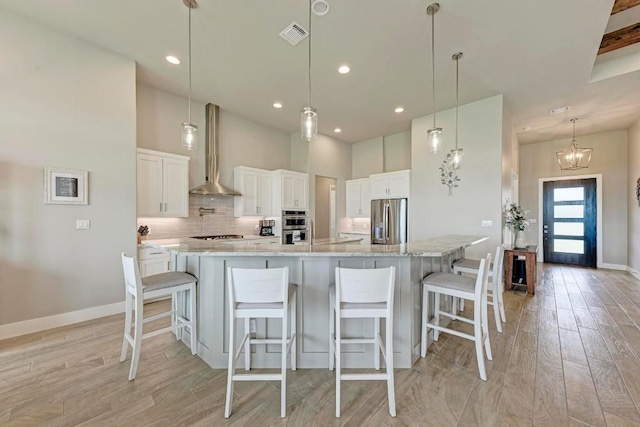 kitchen featuring appliances with stainless steel finishes, light wood-type flooring, wall chimney range hood, decorative light fixtures, and white cabinetry