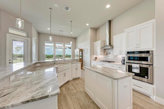 kitchen featuring light stone counters, white cabinets, and wall chimney range hood