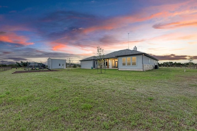 back house at dusk featuring a lawn and a shed