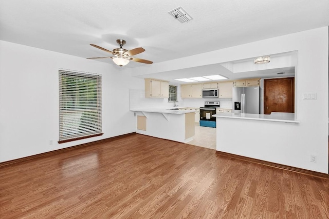 kitchen with ceiling fan with notable chandelier, light wood-type flooring, cream cabinetry, kitchen peninsula, and stainless steel appliances