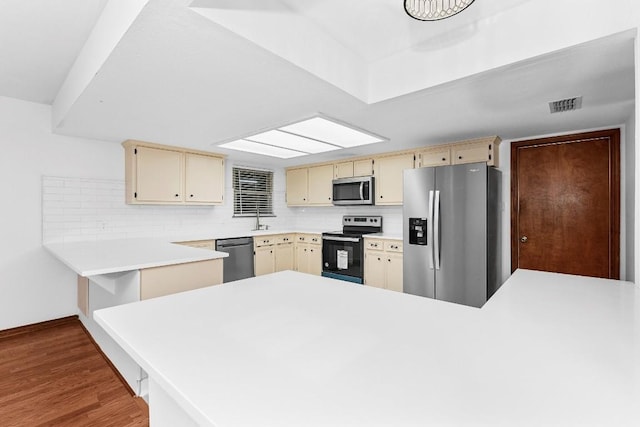 kitchen featuring kitchen peninsula, backsplash, stainless steel appliances, wood-type flooring, and cream cabinets