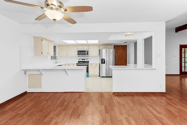 kitchen with kitchen peninsula, appliances with stainless steel finishes, sink, cream cabinets, and light hardwood / wood-style flooring