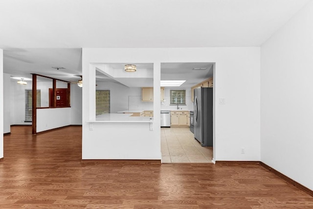 kitchen with kitchen peninsula, appliances with stainless steel finishes, backsplash, and light hardwood / wood-style flooring