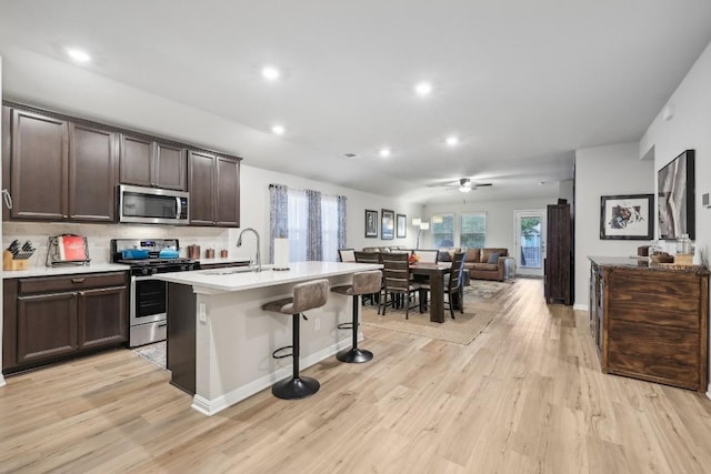 kitchen featuring sink, light wood-type flooring, an island with sink, and appliances with stainless steel finishes