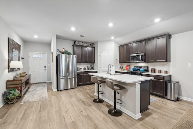 kitchen with sink, an island with sink, stainless steel appliances, and light wood-type flooring