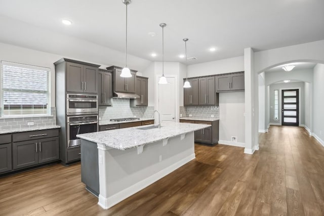 kitchen featuring light stone countertops, sink, pendant lighting, a kitchen island with sink, and appliances with stainless steel finishes