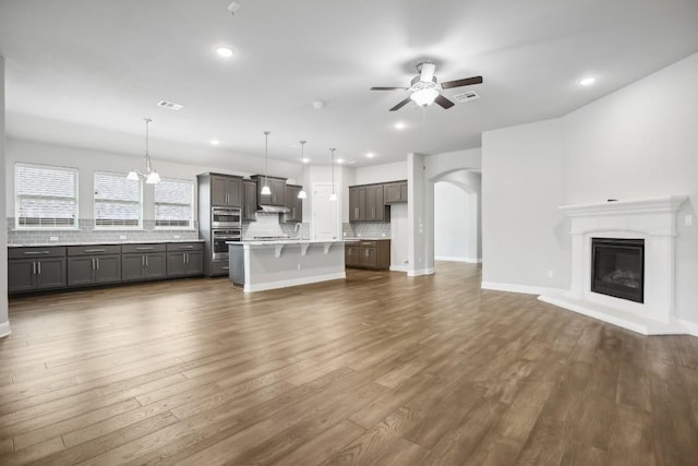 unfurnished living room featuring ceiling fan with notable chandelier and dark wood-type flooring