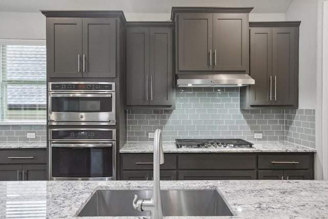 kitchen featuring decorative backsplash, stainless steel appliances, light stone counters, and sink