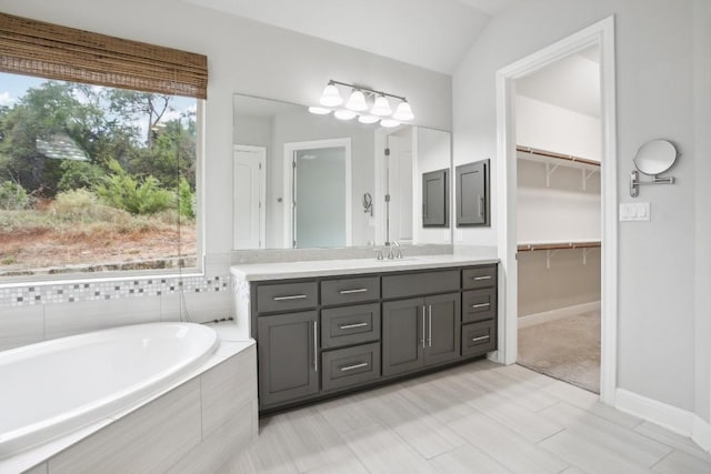 bathroom with vanity, a relaxing tiled tub, and vaulted ceiling