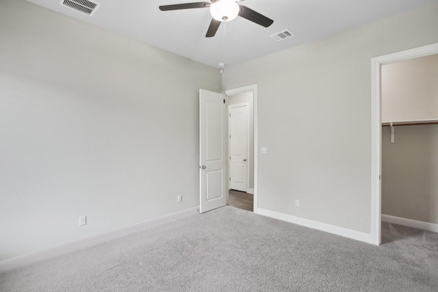 unfurnished bedroom with a walk in closet, ceiling fan, a closet, and dark carpet