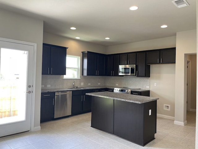 kitchen featuring light stone countertops, stainless steel appliances, sink, light tile patterned floors, and a center island