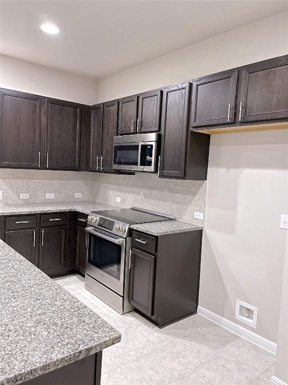 kitchen with dark brown cabinetry, decorative backsplash, light stone countertops, and appliances with stainless steel finishes