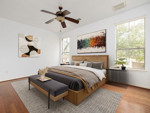 bedroom with visible vents, light wood-style flooring, radiator heating unit, a ceiling fan, and baseboards