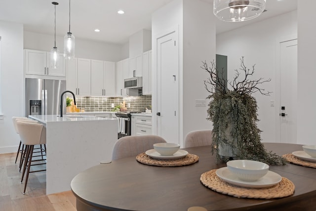 kitchen featuring light wood-type flooring, stainless steel appliances, sink, pendant lighting, and white cabinetry