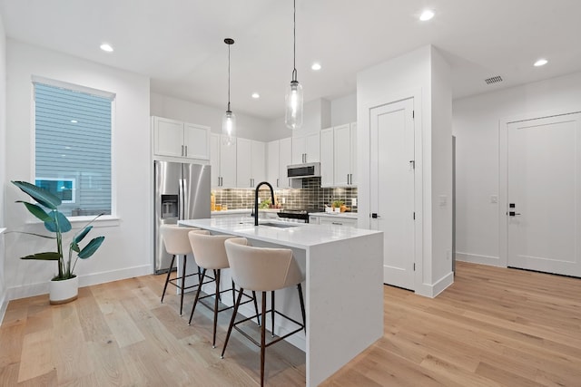 kitchen featuring white cabinets, appliances with stainless steel finishes, light hardwood / wood-style floors, and a kitchen island with sink