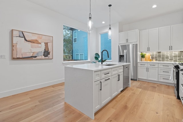 kitchen featuring stainless steel appliances, light hardwood / wood-style flooring, white cabinetry, hanging light fixtures, and an island with sink