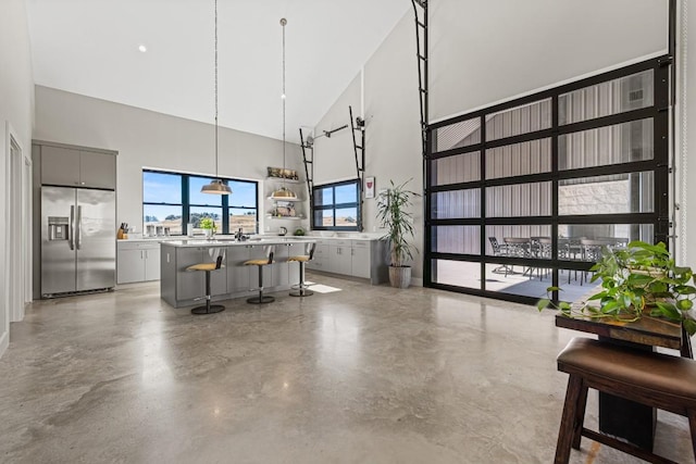 kitchen featuring gray cabinetry, a high ceiling, stainless steel fridge with ice dispenser, a breakfast bar, and a kitchen island