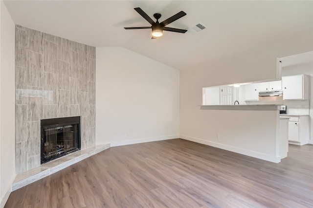 unfurnished living room with ceiling fan, lofted ceiling, a tiled fireplace, and light hardwood / wood-style flooring