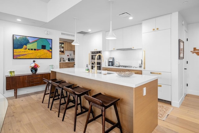 70 Rainey St Unit 1306, Austin, TX 78701 - kitchen featuring a sink, a kitchen breakfast bar, stainless steel double oven, light wood-style flooring, and a center island with sink