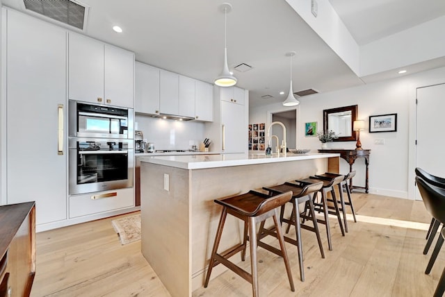 70 Rainey St Unit 1306, Austin, TX 78701 - kitchen with stainless steel double oven, light wood finished floors, light countertops, recessed lighting, and hanging light fixtures