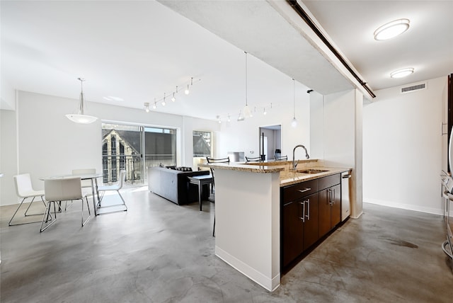 kitchen with light stone countertops, a kitchen island with sink, dark brown cabinetry, and decorative light fixtures